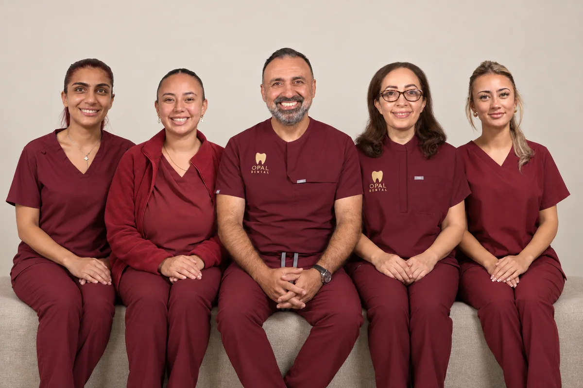 Five members of the Opal Dental team sitting side by side in a studio group portrait, all smiling, in burgundy uniforms
